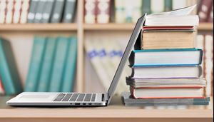 SIS Wordfinder Bärbardator står på ett bord med en trave med böcker bakom